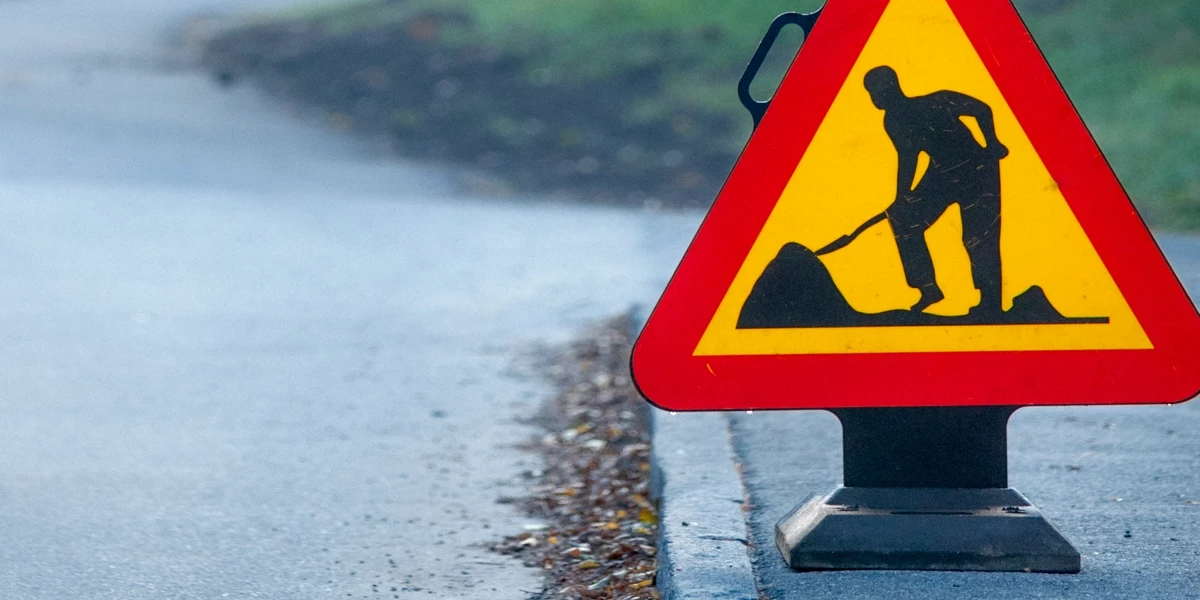 En kvinna korsar en gata vid en skylt som varnar för vägarbete.