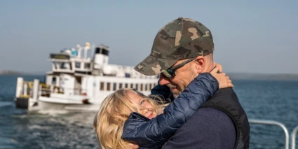 En man och en flicka omfamnar varandra på en kaj med en skärgårdsbåt i bakgrunden.