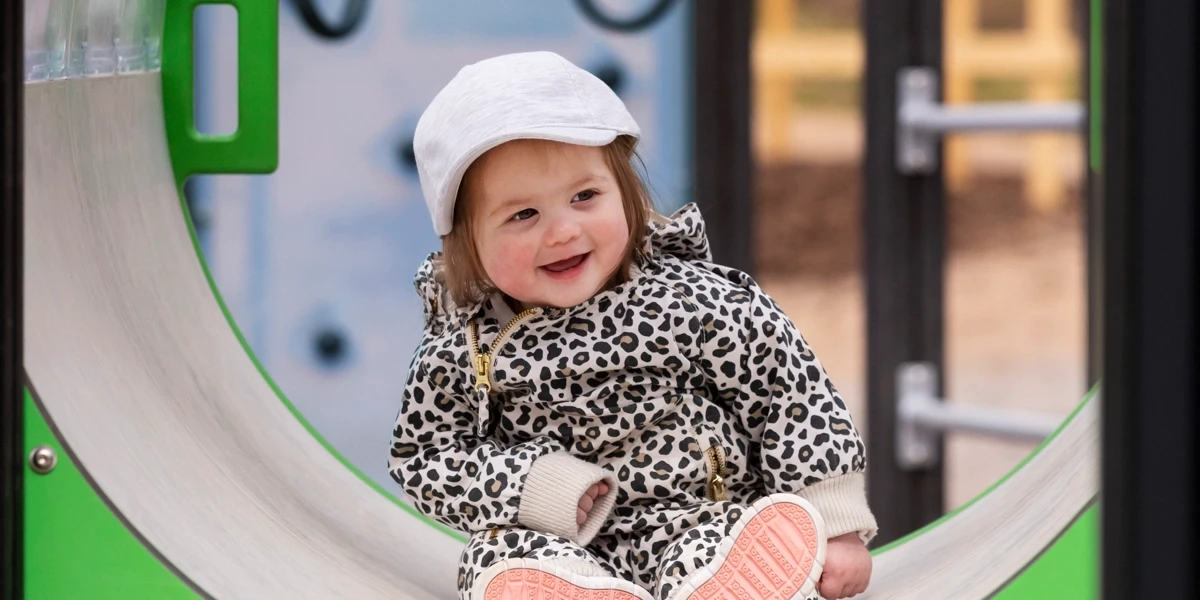 En liten flicka sitter i en klätterställning på en lekplats. 